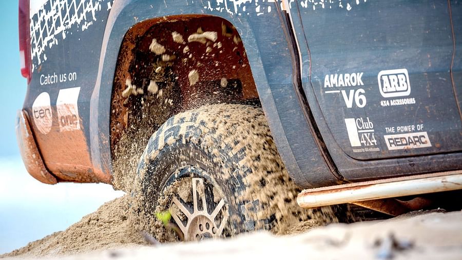 Split image of a vehicle driving on a beach and a vehicle driving over a sand dune